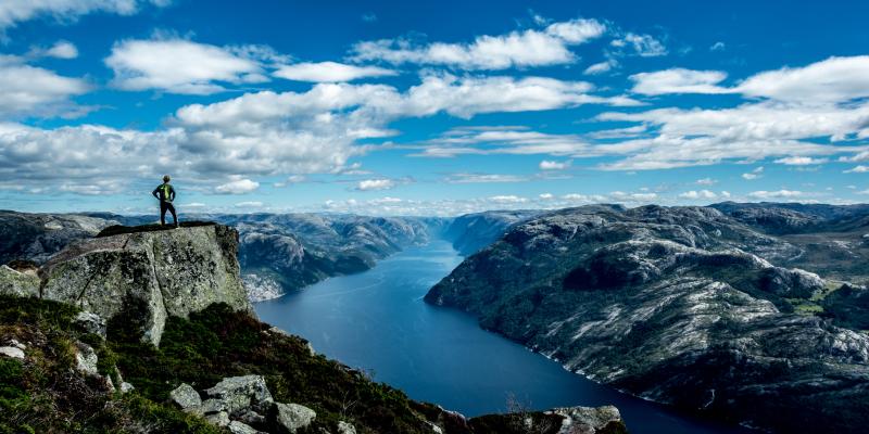 Mann på fjelltopp ser ut over fjord